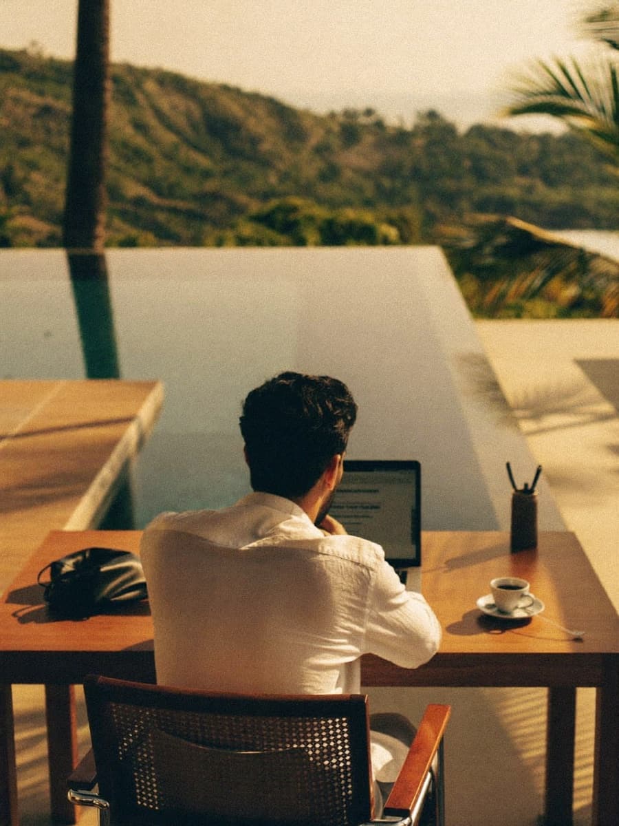A founder working from a laptop at a poolside desk overlooking forested hills